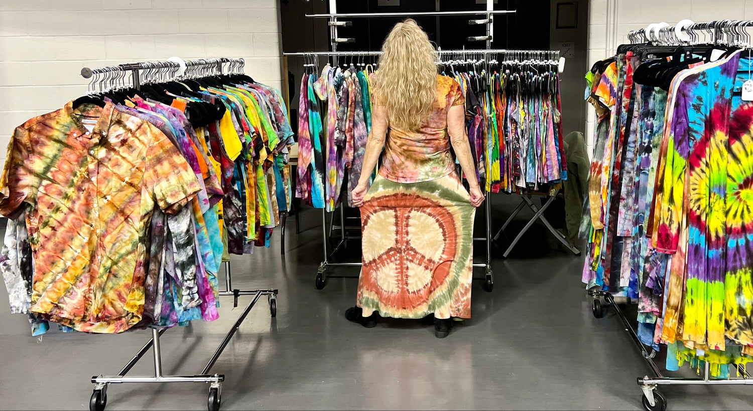 Person wearing a tie-dye dress in a store with tie-dye clothing on display.